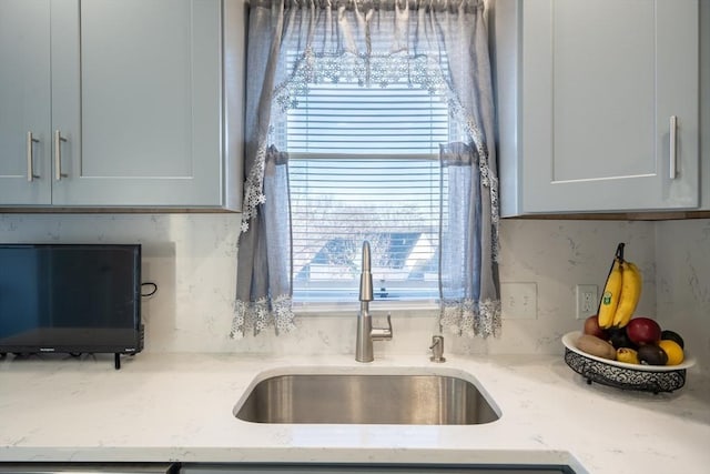 kitchen with light stone counters, a healthy amount of sunlight, a sink, and backsplash