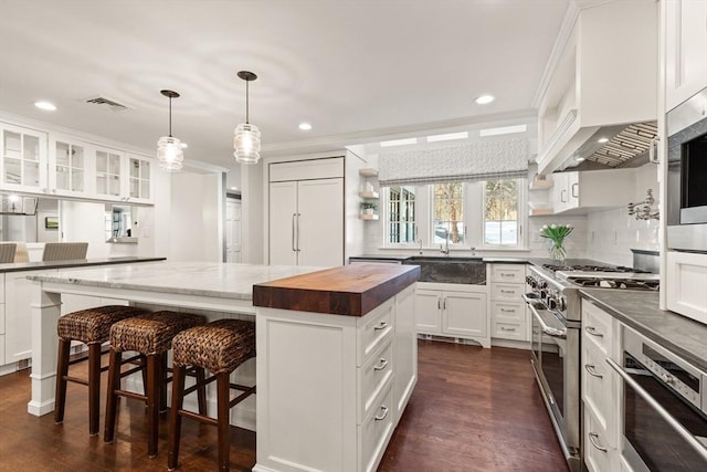 kitchen featuring a breakfast bar, white cabinetry, butcher block counters, high end appliances, and a kitchen island