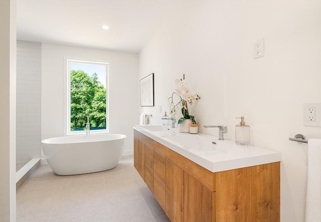 full bath featuring double vanity, a freestanding tub, tile patterned flooring, and a sink