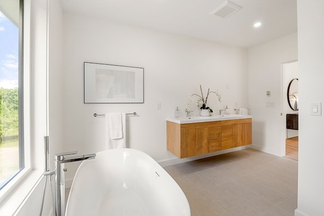 bathroom with tile floors, dual bowl vanity, a bath to relax in, and a wealth of natural light