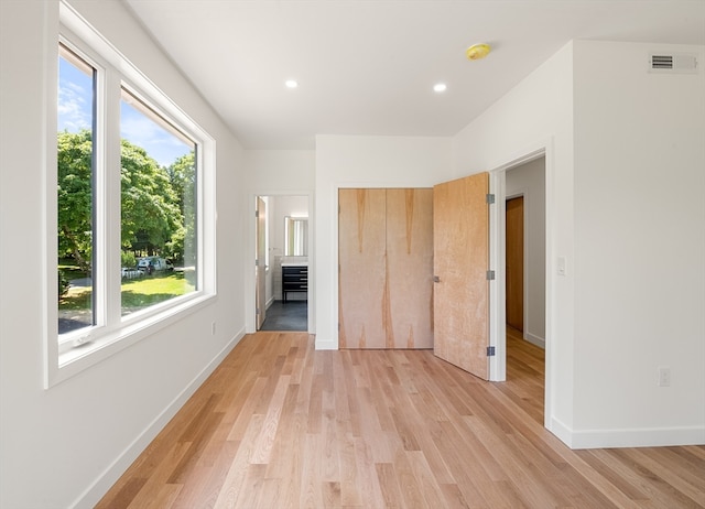 unfurnished bedroom with multiple windows, light hardwood / wood-style flooring, and connected bathroom