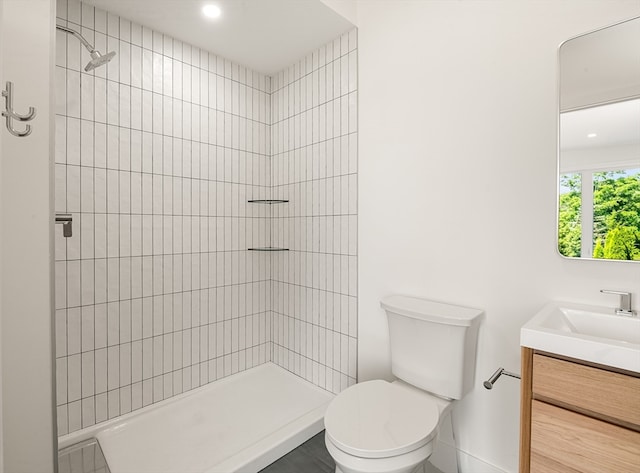 bathroom with a tile shower, vanity, and toilet