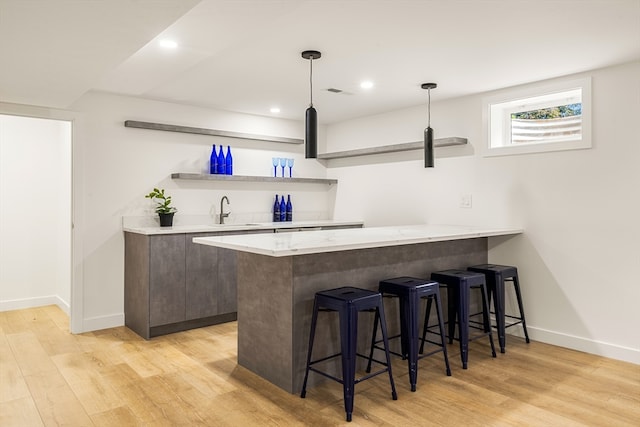 bar with light hardwood / wood-style floors, light stone countertops, dark brown cabinets, sink, and pendant lighting