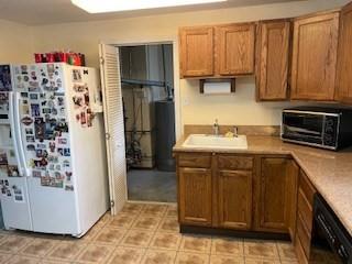 kitchen featuring freestanding refrigerator, black dishwasher, a sink, light countertops, and brown cabinets