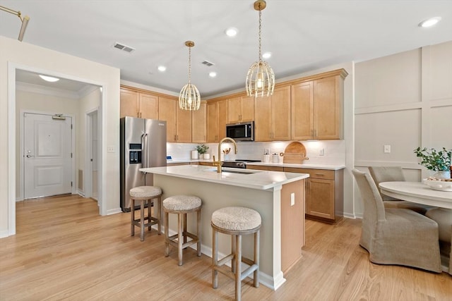 kitchen featuring a kitchen island with sink, hanging light fixtures, sink, light hardwood / wood-style floors, and stainless steel appliances