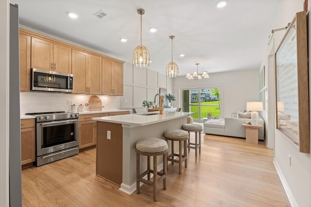 kitchen with sink, stainless steel appliances, a kitchen island with sink, and light hardwood / wood-style flooring