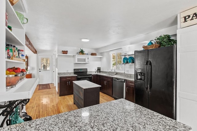 kitchen featuring dark brown cabinetry, sink, light stone counters, a center island, and black appliances