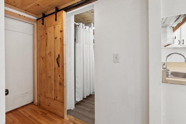 hallway with a barn door, sink, wood ceiling, and light wood-type flooring