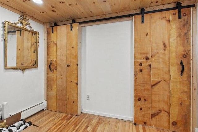 interior space with a barn door, baseboard heating, and light wood-type flooring