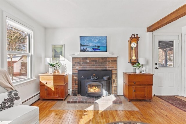 living room featuring a fireplace, beam ceiling, light hardwood / wood-style flooring, and a baseboard heating unit