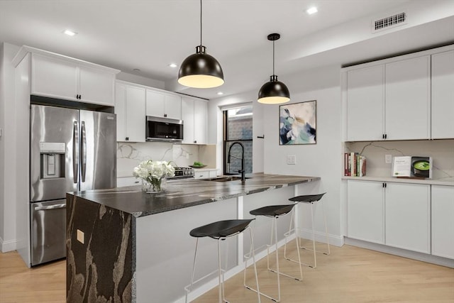 kitchen with visible vents, a sink, tasteful backsplash, stainless steel appliances, and light wood-style floors