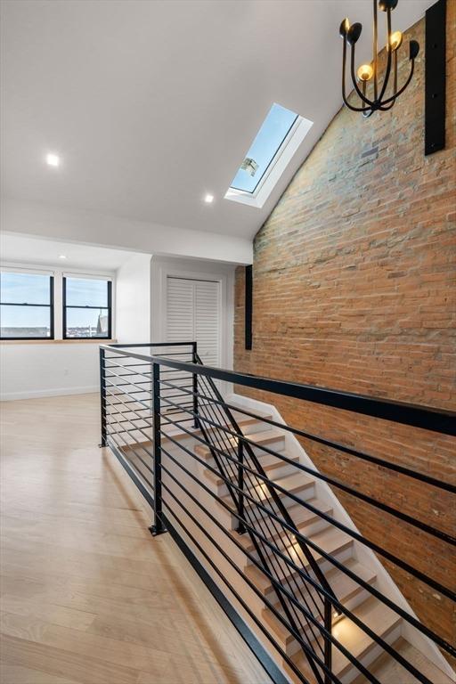 corridor featuring a skylight, an upstairs landing, high vaulted ceiling, and wood finished floors