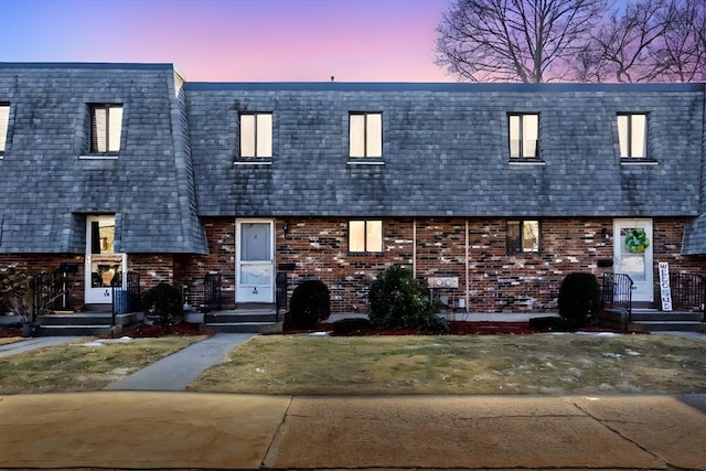 view of property with mansard roof, brick siding, and roof with shingles