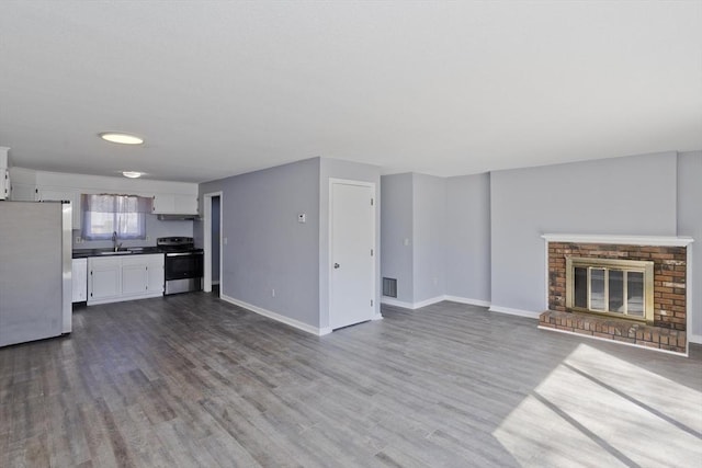 unfurnished living room with dark wood-style floors, visible vents, baseboards, and a sink