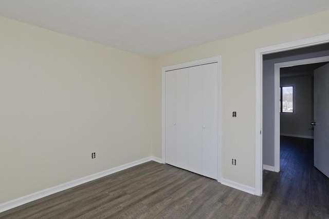 unfurnished bedroom featuring dark wood finished floors, a closet, and baseboards