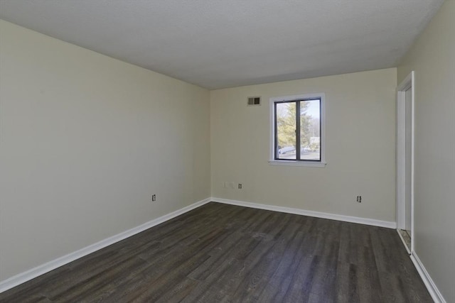 unfurnished room with dark wood-style floors, visible vents, and baseboards