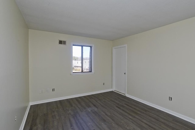 empty room featuring dark wood-type flooring, baseboards, and visible vents