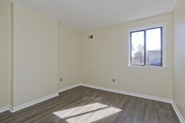 empty room with dark wood-style floors, visible vents, and baseboards