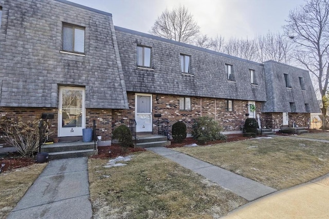 view of front of house with a front yard, mansard roof, and brick siding