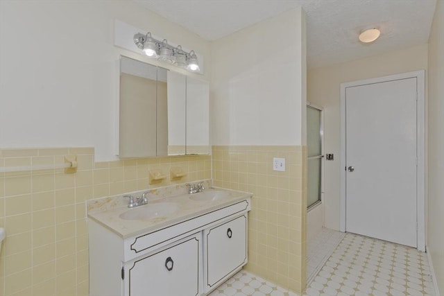 bathroom with bath / shower combo with glass door, wainscoting, tile walls, and a sink