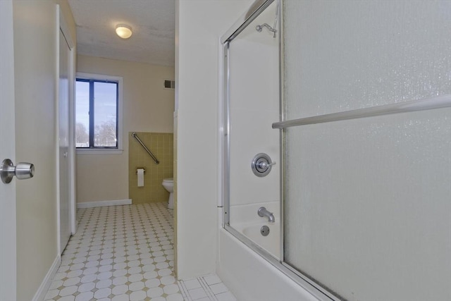 bathroom featuring tile walls, toilet, visible vents, and shower / bath combination with glass door