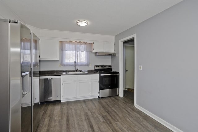 kitchen featuring a sink, under cabinet range hood, appliances with stainless steel finishes, white cabinetry, and dark countertops