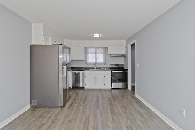 kitchen with a sink, dark countertops, white cabinetry, stainless steel appliances, and light wood finished floors