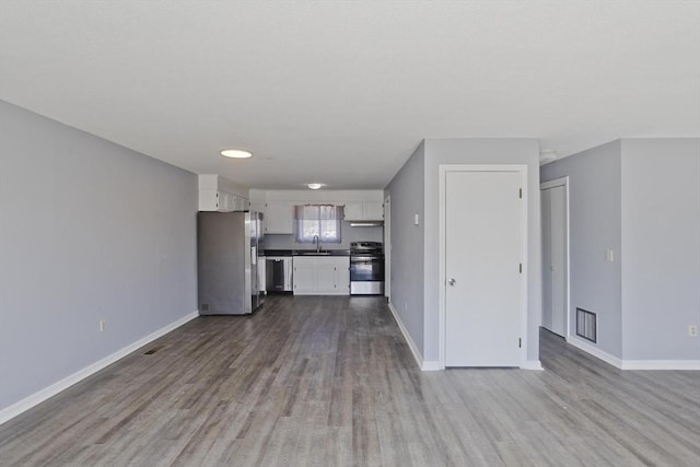 unfurnished living room with a sink, visible vents, baseboards, and dark wood-style flooring