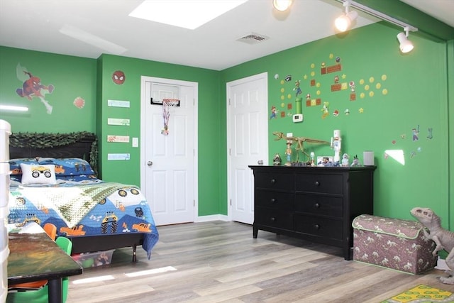 bedroom with a skylight, visible vents, baseboards, and wood finished floors