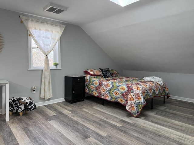 bedroom featuring lofted ceiling with skylight, wood finished floors, visible vents, and baseboards