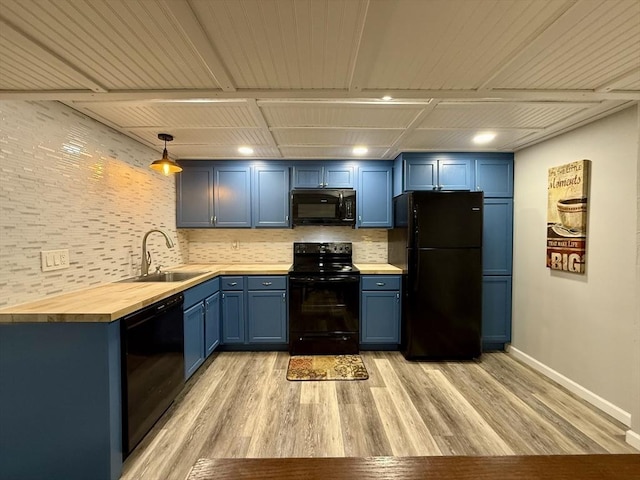 kitchen featuring blue cabinets, black appliances, a sink, wood counters, and light wood finished floors