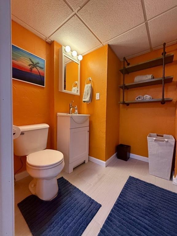 bathroom with a drop ceiling, toilet, vanity, and baseboards