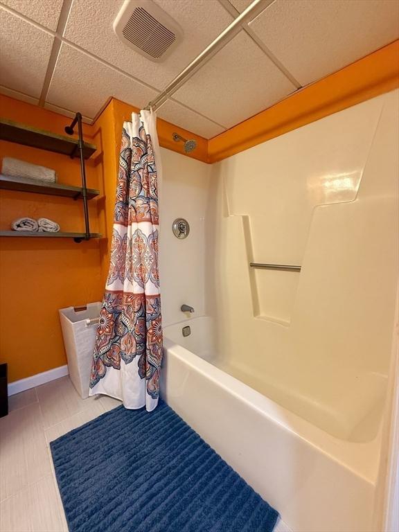 bathroom with a drop ceiling, visible vents, shower / bath combo with shower curtain, and baseboards