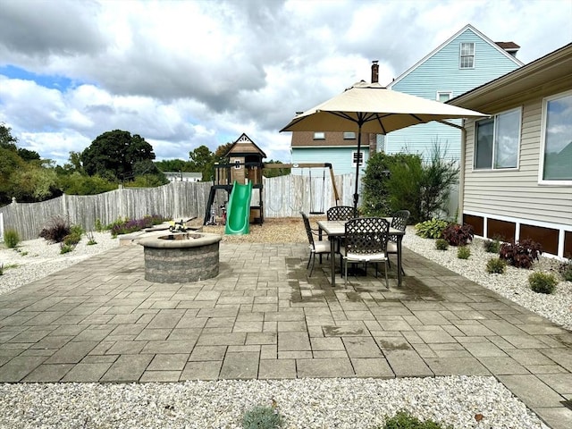 view of patio / terrace with outdoor dining area, an outdoor fire pit, a playground, and fence