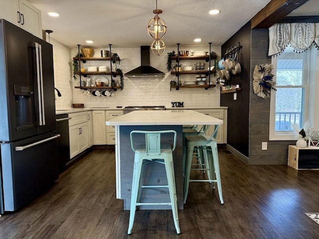 interior space with wall chimney range hood, dark wood-style floors, backsplash, and black refrigerator with ice dispenser