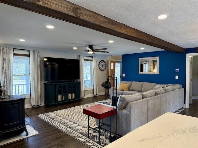 living area with beam ceiling, dark wood-style floors, a wood stove, and a wealth of natural light