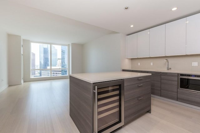 kitchen featuring light countertops, white cabinets, a sink, modern cabinets, and beverage cooler