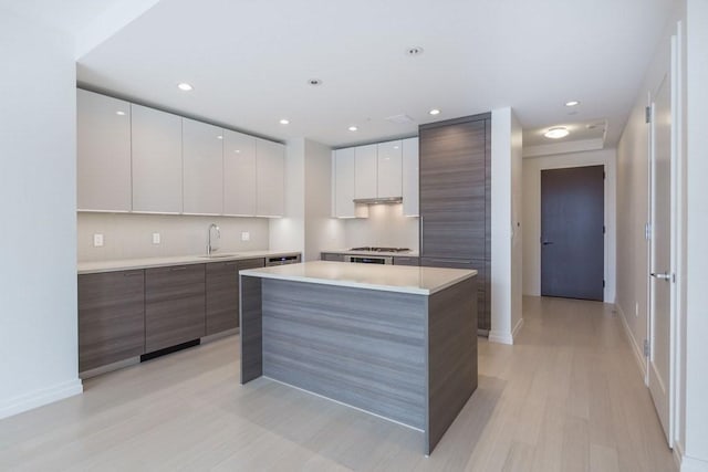 kitchen featuring light countertops, white cabinets, a kitchen island, a sink, and modern cabinets