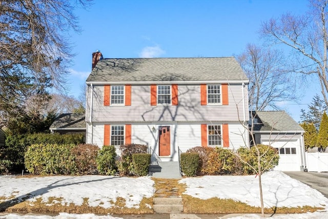 colonial inspired home with driveway, a chimney, roof with shingles, an attached garage, and fence