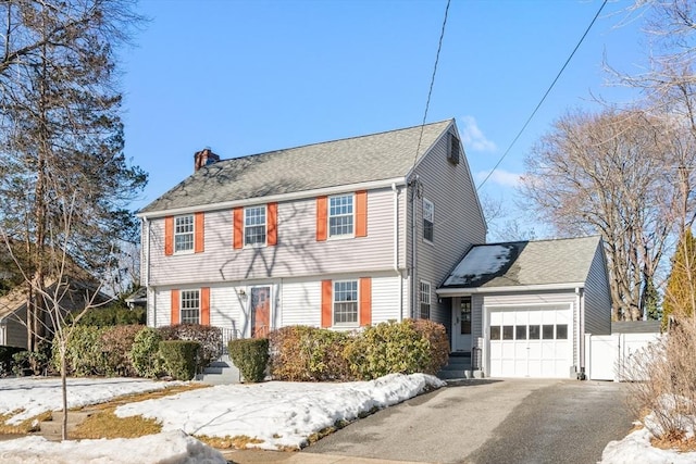 colonial home with aphalt driveway, fence, a chimney, and an attached garage