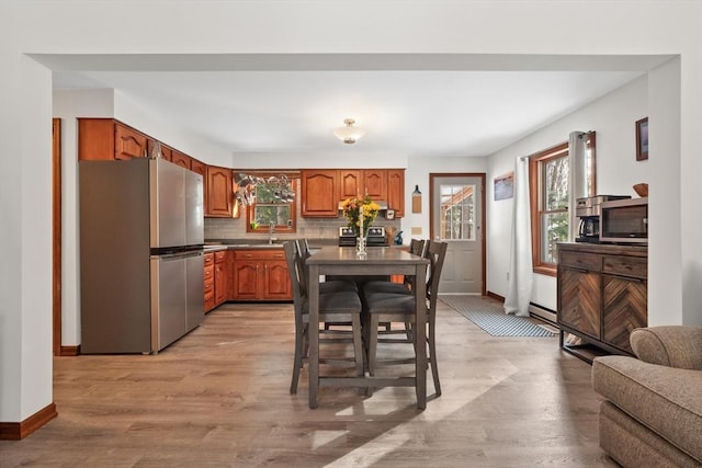 kitchen featuring baseboard heating, appliances with stainless steel finishes, decorative backsplash, sink, and light wood-type flooring