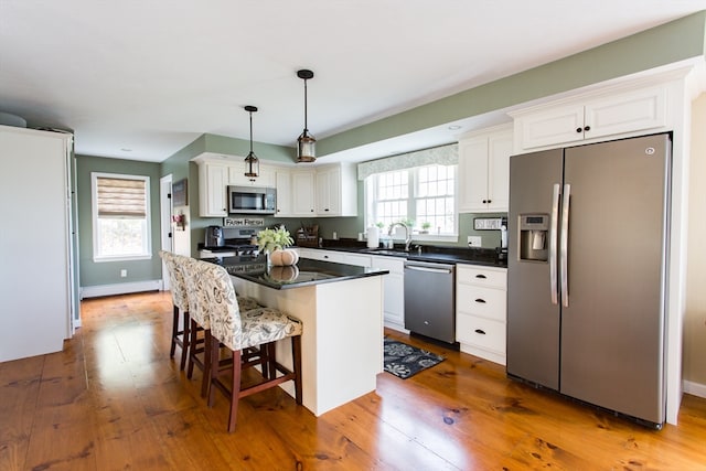 kitchen featuring stainless steel appliances, white cabinetry, decorative light fixtures, hardwood / wood-style floors, and a center island