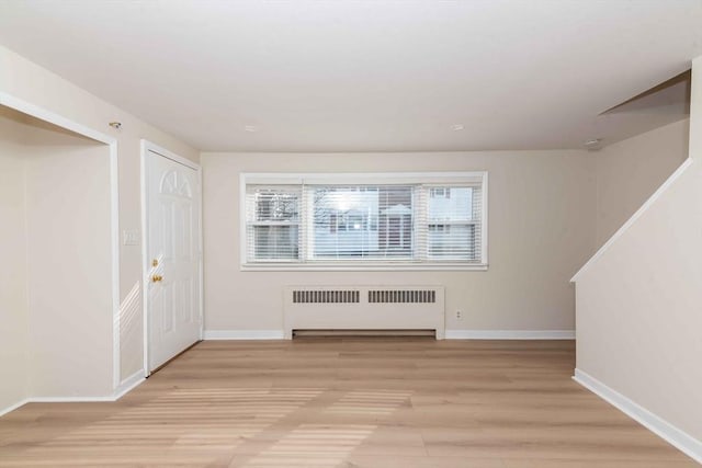 foyer entrance with radiator heating unit, light wood-style floors, and baseboards