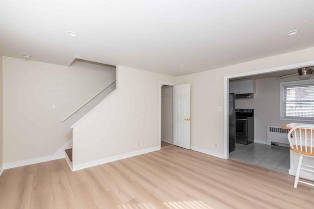 unfurnished living room featuring stairway, radiator heating unit, light wood-style flooring, and baseboards