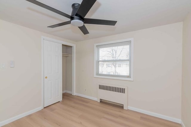 unfurnished bedroom with radiator, baseboards, ceiling fan, light wood-style floors, and a closet