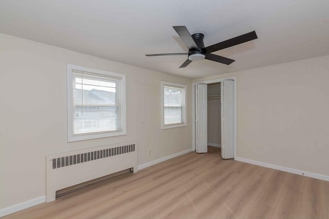 unfurnished bedroom featuring ceiling fan, baseboards, radiator, and light wood-style flooring