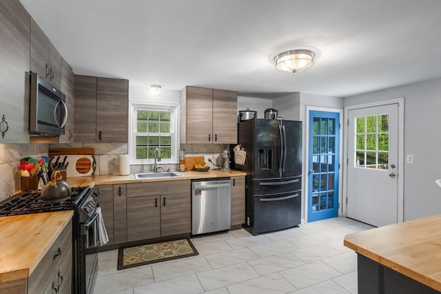 kitchen with black appliances, a sink, butcher block countertops, and decorative backsplash