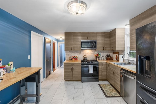 kitchen featuring black appliances, a sink, butcher block countertops, light marble finish flooring, and decorative backsplash
