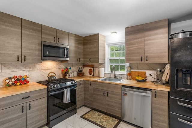 kitchen featuring black appliances, wooden counters, a sink, and backsplash