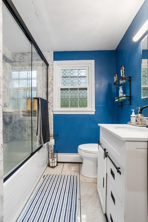 bathroom featuring toilet, vanity, bath / shower combo with glass door, a baseboard heating unit, and marble finish flooring